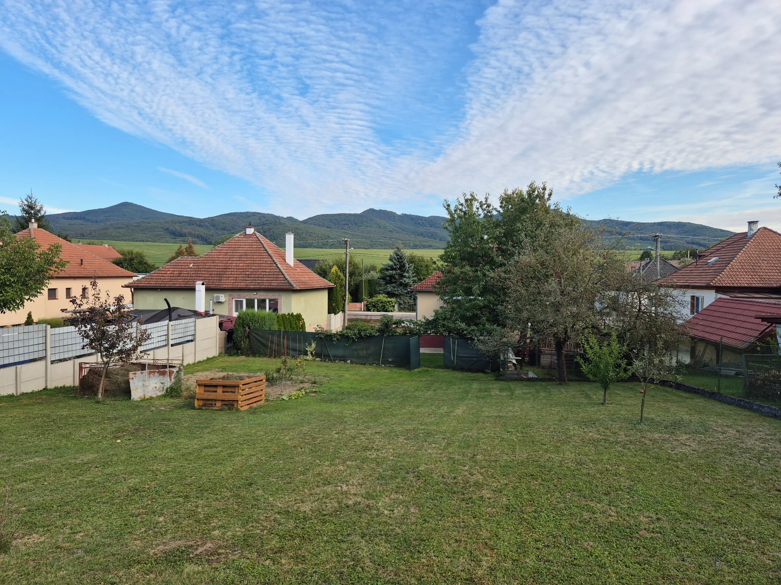 Pohľad z horného konca veľkej záhrady v Soblahove na trávnik, záhon a horský horizont ponad domy